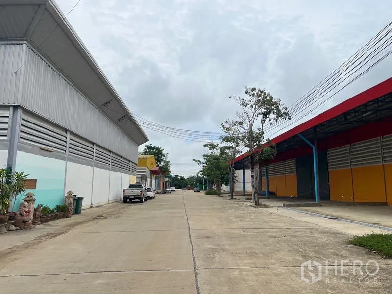 Warehouse for rent or sale in Sai Noi, Nonthaburi - Wide concrete access road between warehouse buildings in an industrial estate.
