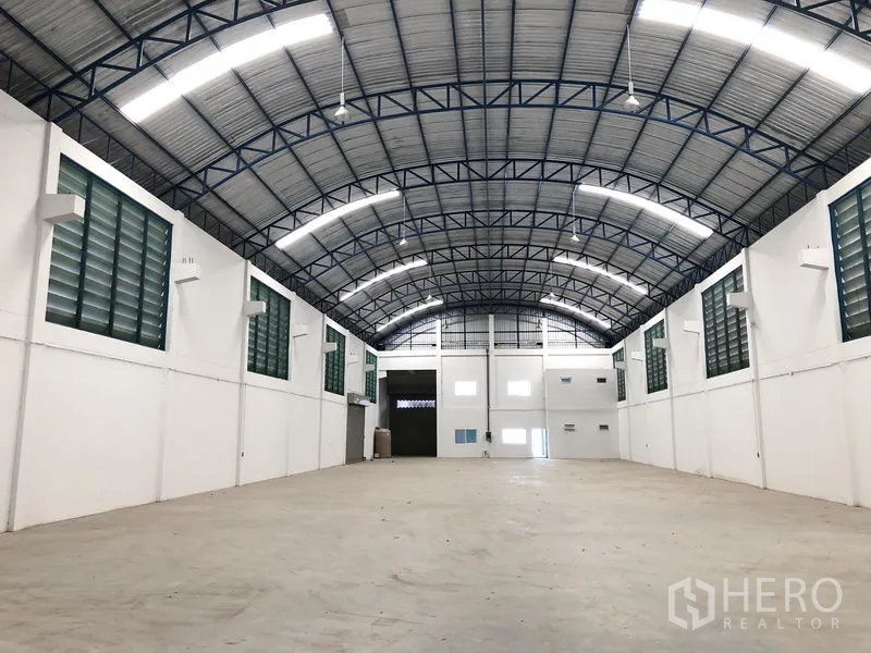 Factory for rent or sale in Bang Sao Thong, Samut Prakan - Spacious warehouse interior featuring a high arched steel roof, bright strip lighting, and concrete floor.
