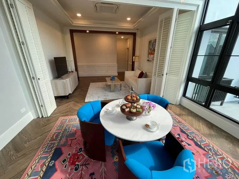 บ้าน ให้เช่าหรือขายในSaphan Sung, Bangkok - ซันรูมสว่างสำหรับนั่งเล่นพร้อมโต๊ะทรงกลม เก้าอี้สีน้ำเงิน และพรมสีชมพูลายกราฟิก