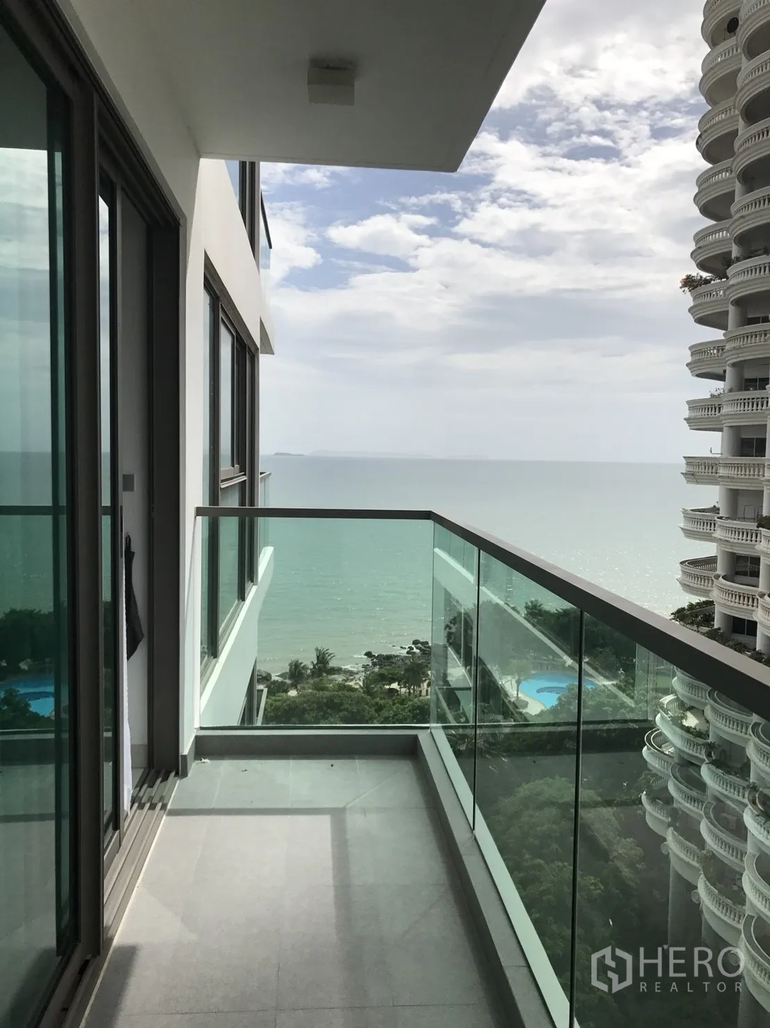 Condominium for rent in Bang Lamung, Chon Buri - Private glass-railed balcony with panoramic sea view over trees and nearby pools.