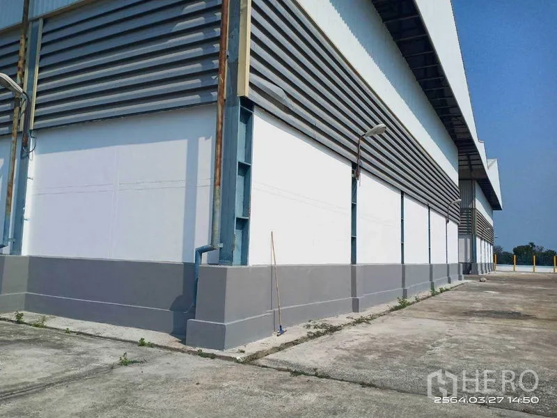 Warehouse for rent in Bang Bo, Samut Prakan - Long side elevation showing cladding, downpipes, and a service walkway.