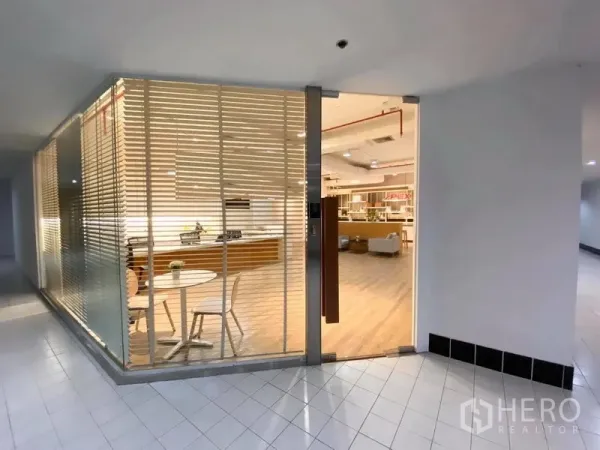 Office Space for rent in Bangkok - Glass-front office entrance with blinds, a small round table and chairs, revealing the reception area inside.