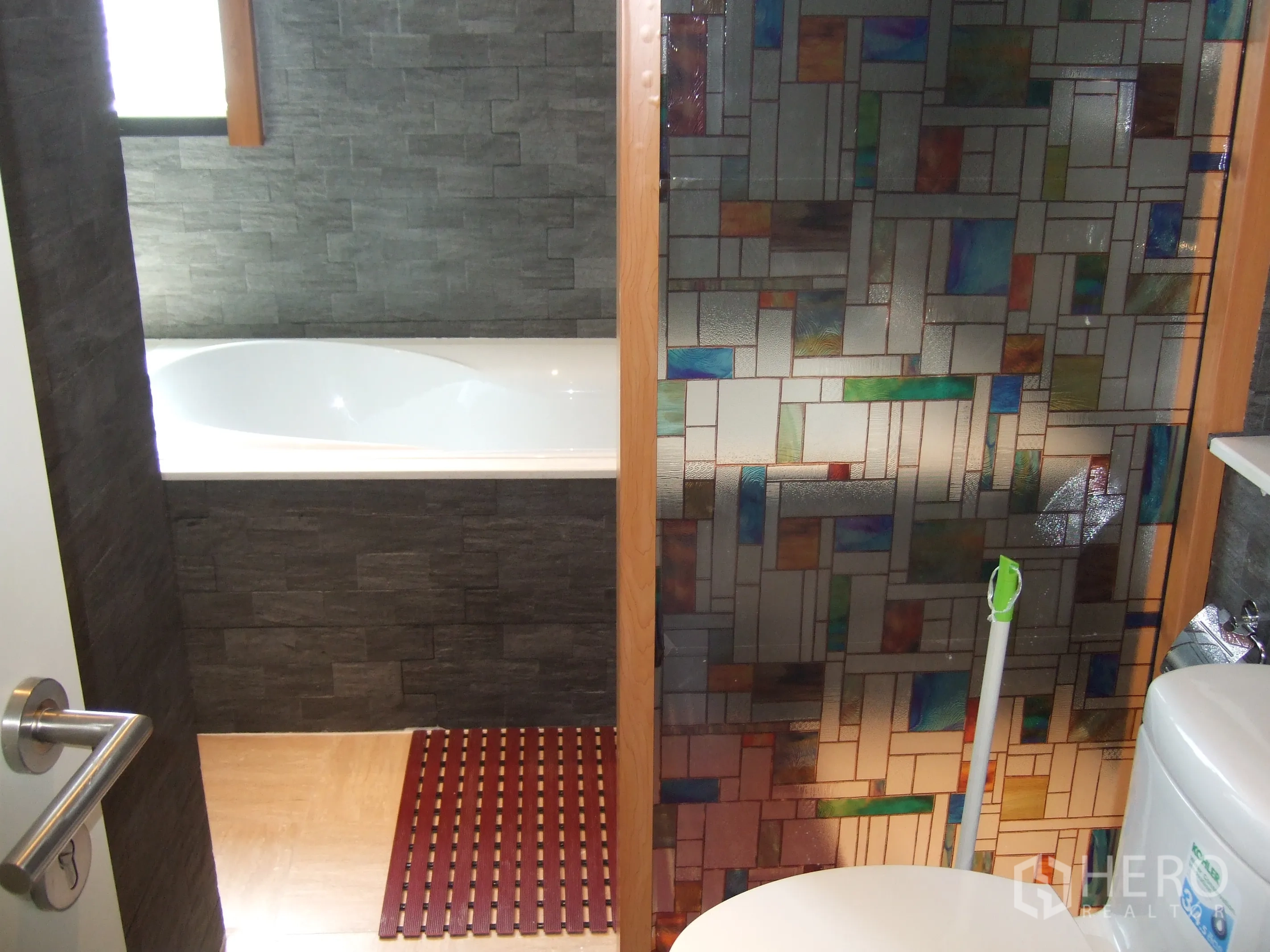 Condominium for rent or sale in Watthana, Bangkok - Modern bathroom with stone tile walls, bathtub, and colorful glass partition.