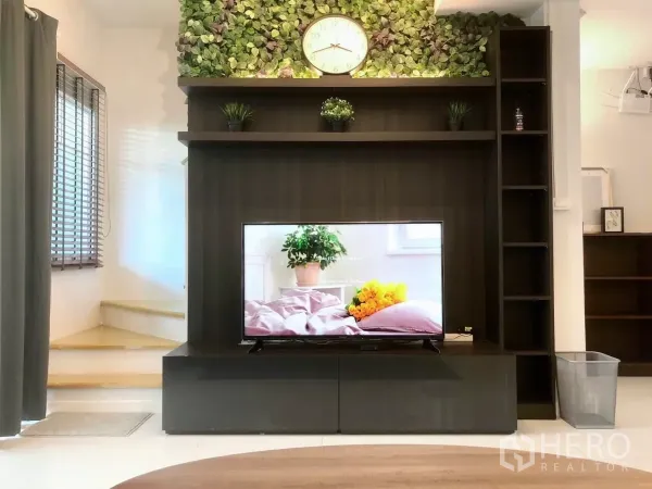 Townhouse for rent or sale in Bang Phli, Samut Prakan - TV wall with dark wood cabinet, floating shelves, greenery feature and wall clock beside the stair.
