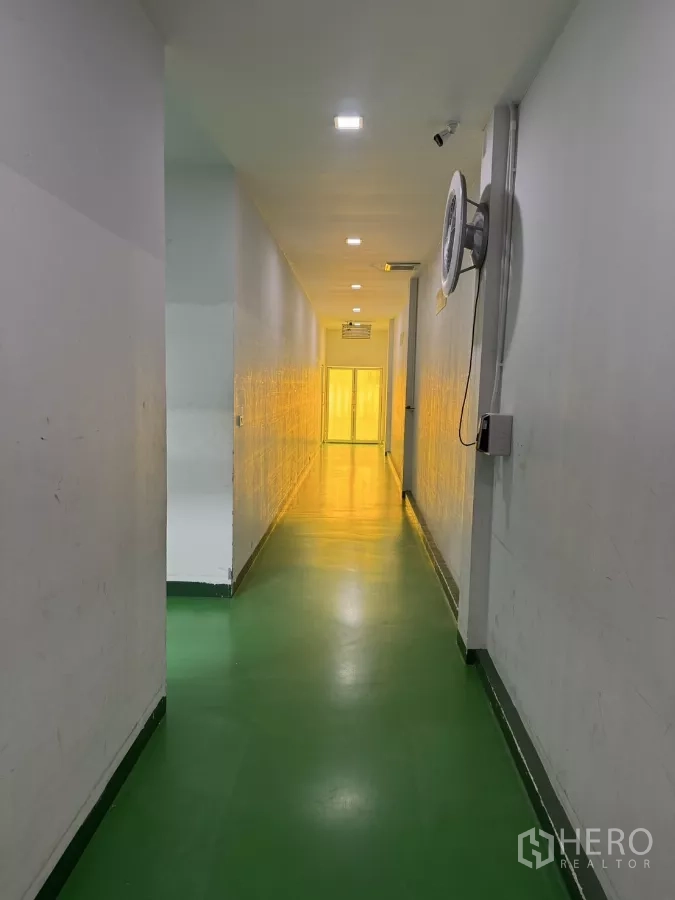 Factory for sale in Lam Luk Ka, Pathum Thani - Industrial hallway with green epoxy floor, wall fan and yellow-lit section ahead.