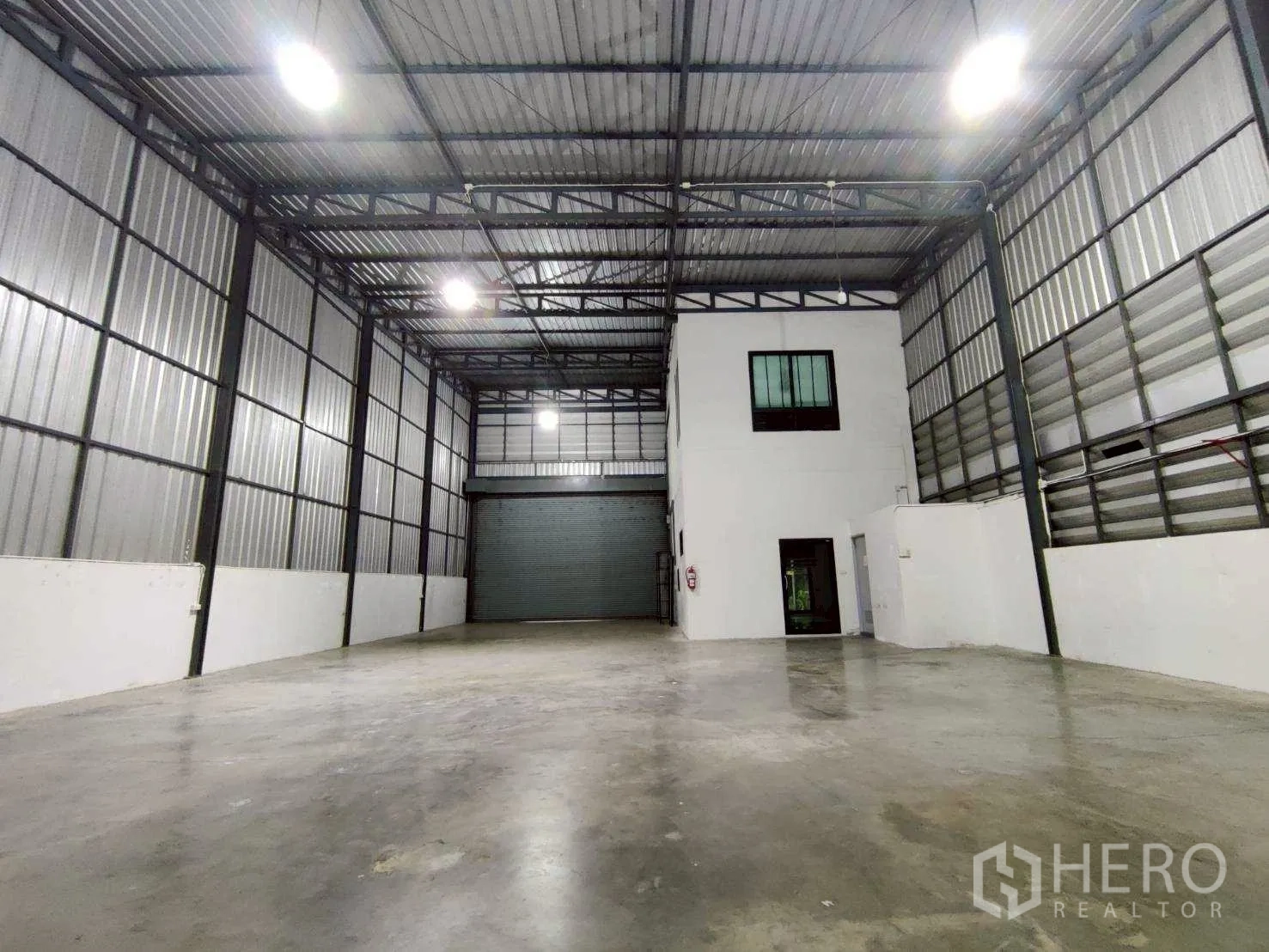 Warehouse for rent in Lam Luk Ka, Pathum Thani - Open storage area facing a large roller shutter and two-storey office block.