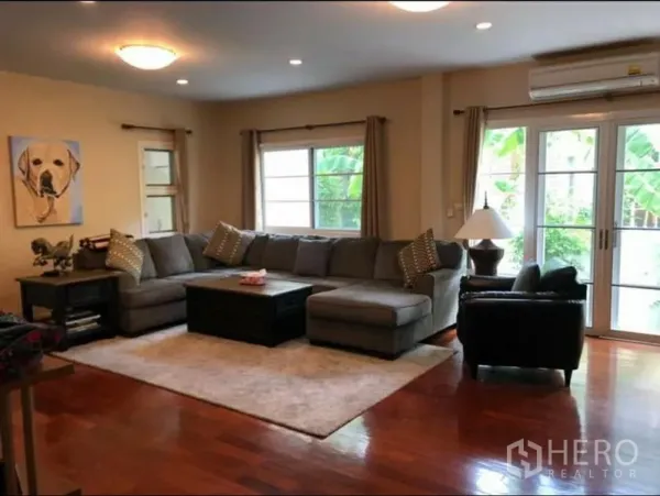 独立式住宅 出租在Phra Khanong, Bangkok - 明亮客厅，转角沙发、木地板、地毯，大窗与推拉玻璃门