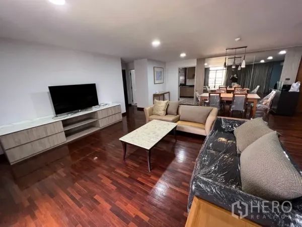 Condominium for rent in Watthana, Bangkok - Spacious living room with hardwood floors, two sofas, TV console and an open dining area with pendant lights.