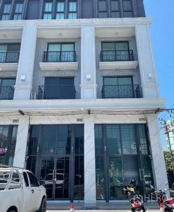 Home Office for rent or sale in Suan Luang, Bangkok - Contemporary 4.5-storey home office façade with tall glass shopfront and upper-floor balconies, with parking area in front.