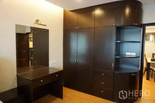 Condominium for rent in Watthana, Bangkok - Dressing area featuring dark wood built‑in wardrobes and a vanity with mirror.