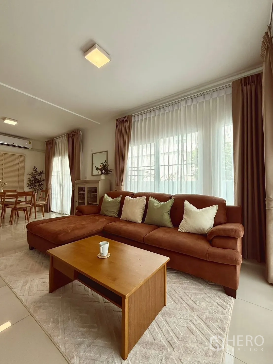 独栋房屋 for rent in Bang Phli, Samut Prakan - 起居区设棕色转角沙发、茶几与落地窗帘。