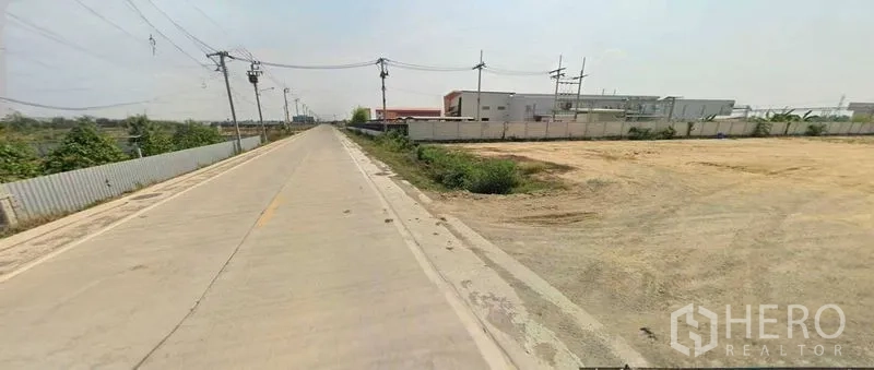 Land for sale in Sai Noi, Nonthaburi - Concrete access road with power poles next to a large vacant land parcel.