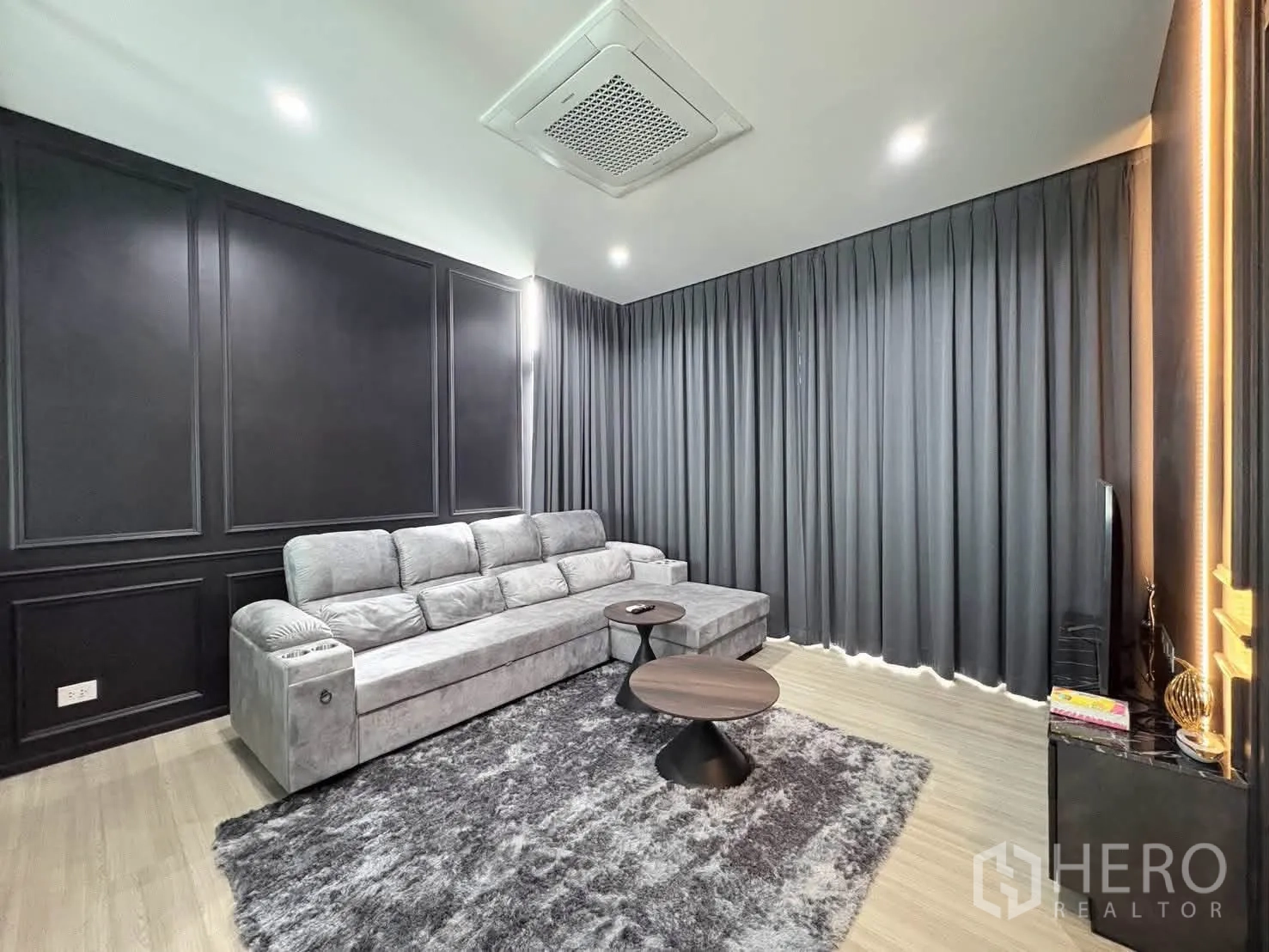 Detached House for rent in Saphan Sung, Bangkok - Family lounge with long gray sofa, area rug, dark feature wall, and blackout curtains.