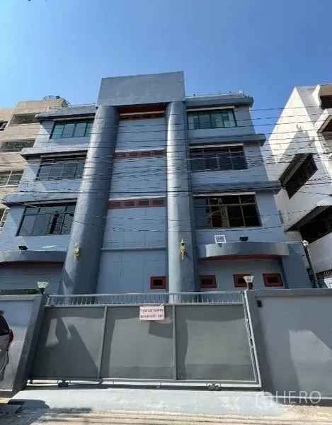 办公空间 出租或出售在Khlong Toei, Bangkok - 曼谷灰色四层办公楼外立面，带围墙与大窗，蓝天下拍摄。