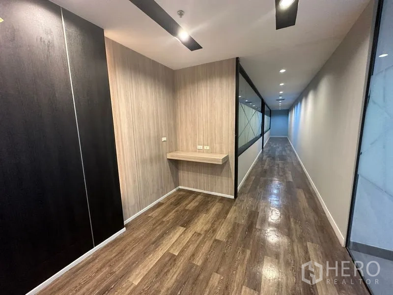 Office Space for rent - Long corridor with built-in wall shelf, wood panels and a glass wall featuring frosted geometric patterns.