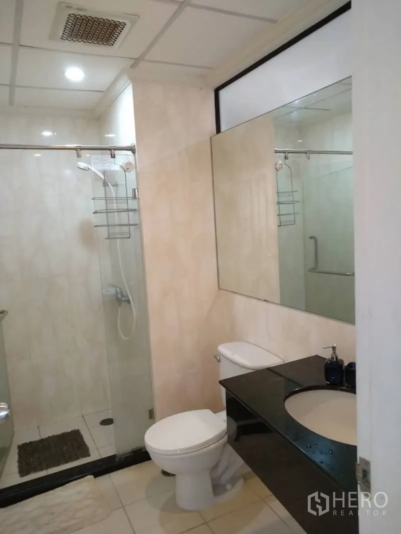 Condominium for rent in Watthana, Bangkok - Modern bathroom with glass-enclosed shower, large mirror and black countertop vanity.