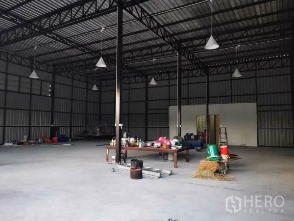 Warehouse for rent - Wide interior shot with multiple hanging lights, a workbench and large open storage area.