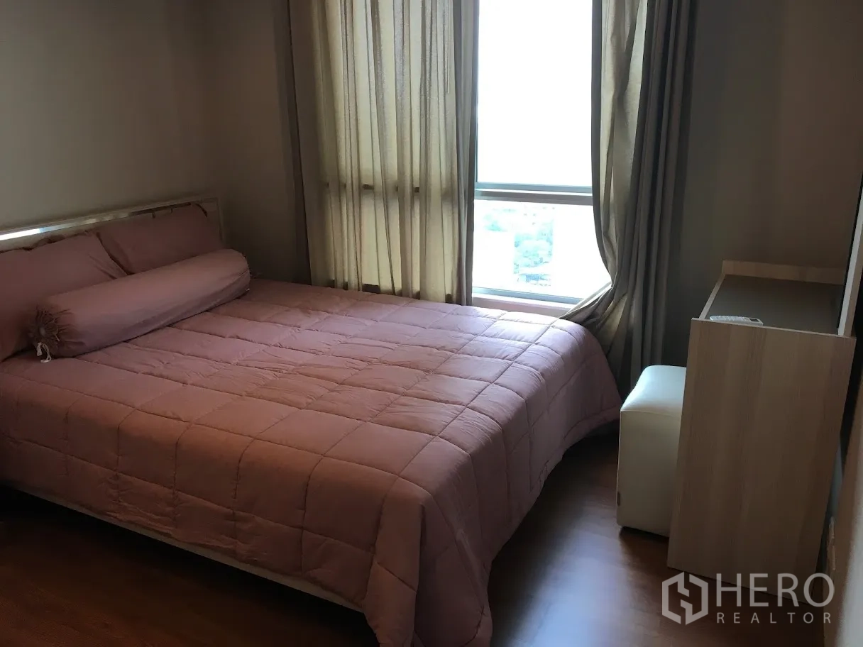 Condominium for rent in Huai Khwang, Bangkok - Cozy bedroom with pink quilted bed, floor-to-ceiling curtains and a window with city view.