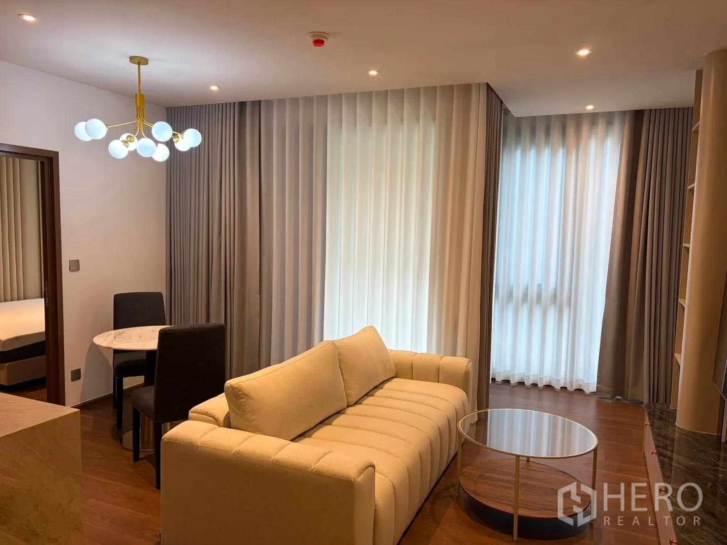 Condominium for rent in Watthana, Bangkok - Open-plan living and dining area showing sofa, TV wall, and light-filled corner windows.