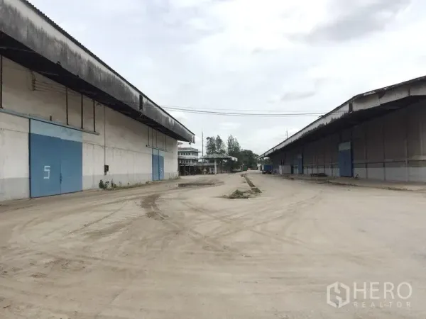 货栈 出租在Pathum Thani - 两座大型混凝土仓库之间的宽阔卡车回转场，配蓝色滑门。