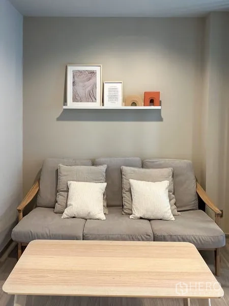Condominium for sale in Ratchathewi, Bangkok - Cozy lounge with gray sofa, throw pillows, wall shelf decor, and a wooden coffee table.