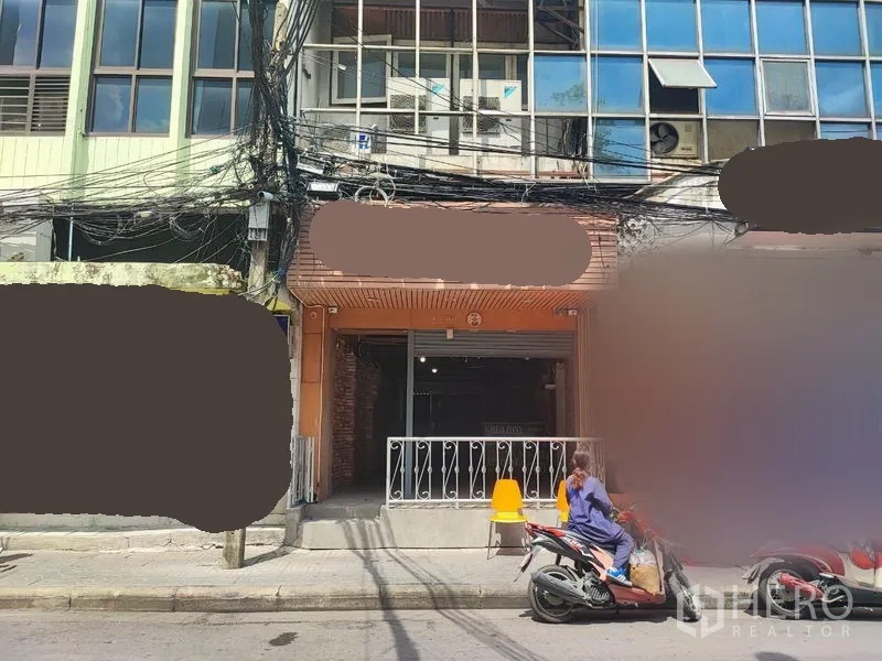Shophouse for rent in Khlong Toei, Bangkok - Street-front shophouse facade with roller shutter, small terrace and motorbikes parked outside.