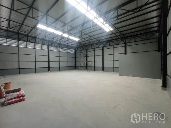 Warehouse for rent in Saphan Sung, Bangkok - Spacious warehouse interior featuring a high steel truss roof with skylights and a smooth concrete floor.