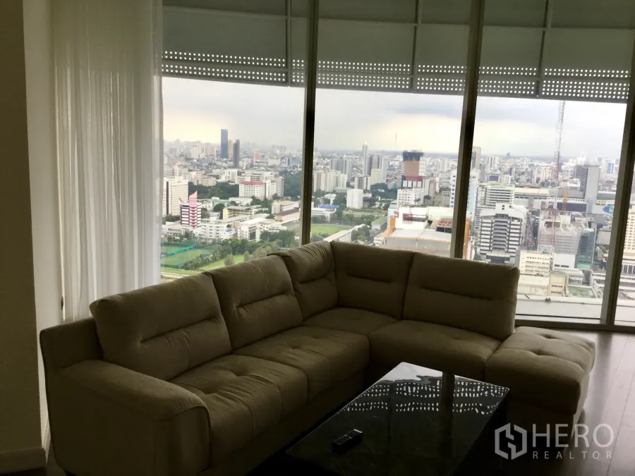 คอนโด ให้เช่าในPathum Wan, Bangkok - ห้องนั่งเล่นสว่างพร้อมโซฟาตัวใหญ่และกระจกเต็มบาน มองเห็นวิวเมืองและสนามกอล์ฟ.