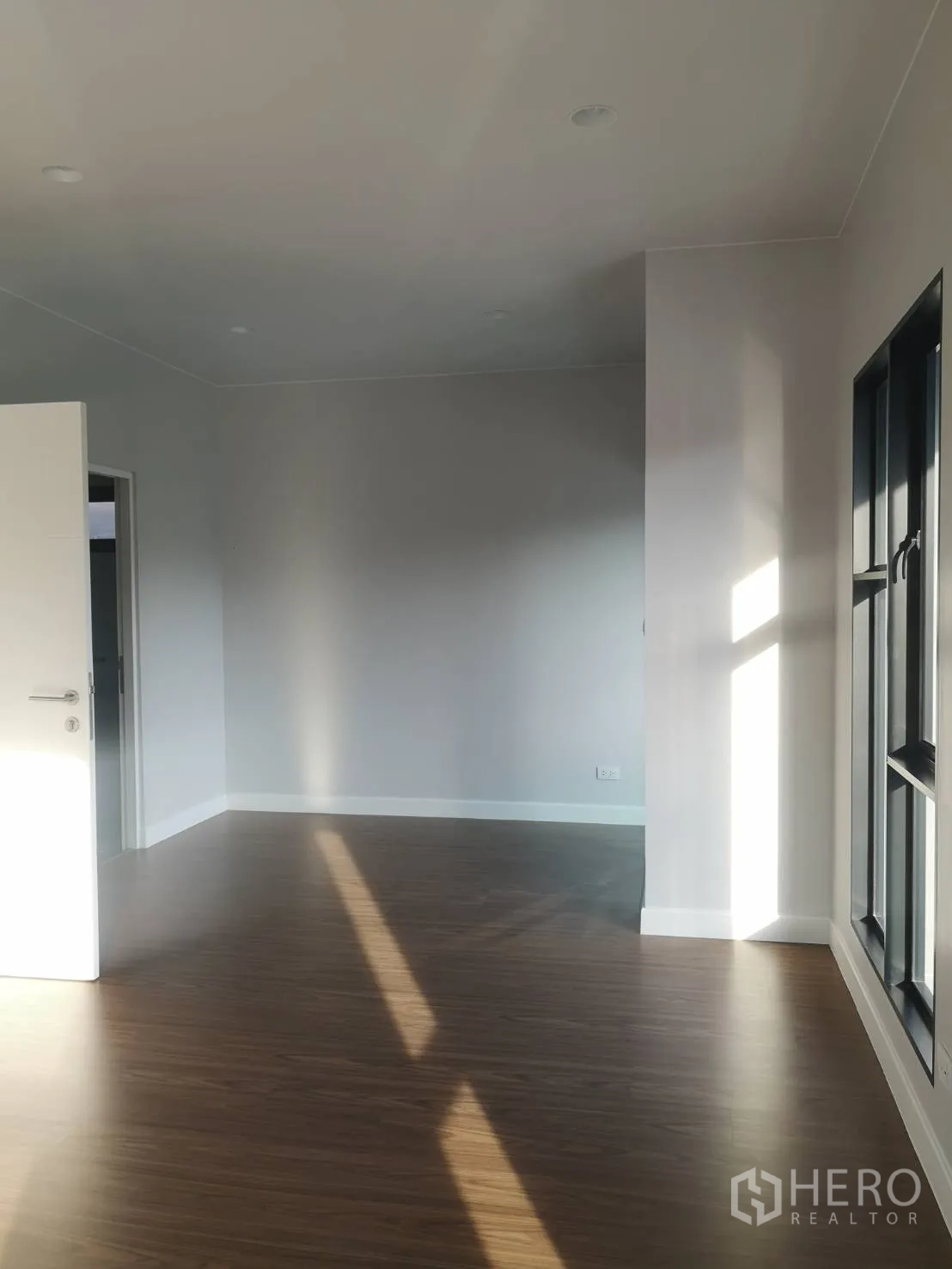 บ้าน ขายในLam Luk Ka, Pathum Thani - ห้องนั่งเล่นโล่งโปร่ง พื้นลายไม้ ผนังสีขาว และหน้าต่างกรอบดำบานใหญ่