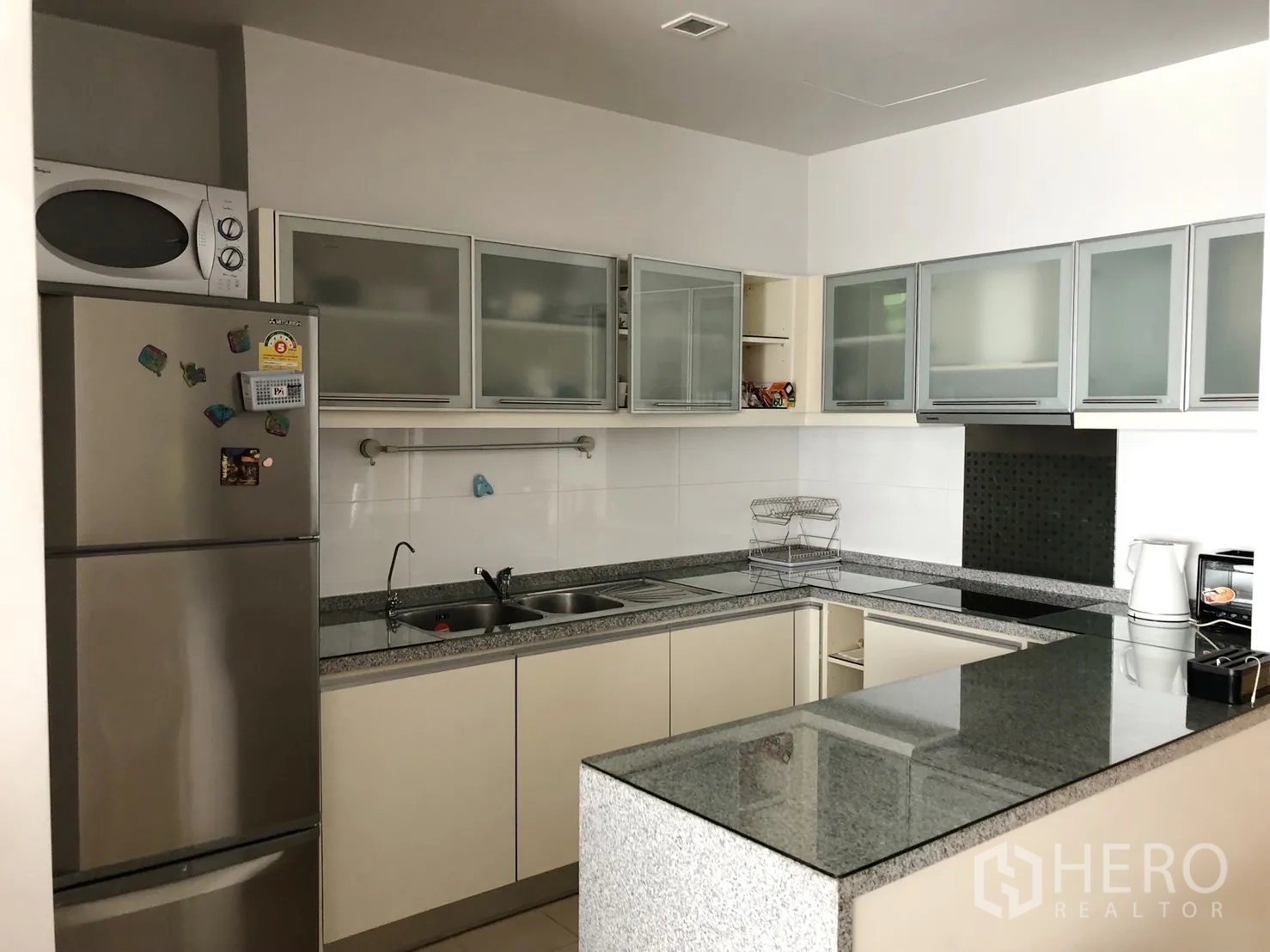 คอนโด ให้เช่าหรือขายในKhlong Toei, Bangkok - ครัวรูปตัว U เคาน์เตอร์หินแกรนิต ตู้บานกระจก และตู้เย็นสแตนเลสพร้อมไมโครเวฟ