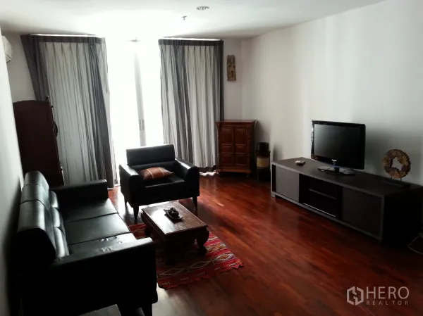 คอนโด ให้เช่าในWatthana, Bangkok - ห้องนั่งเล่นคอนโดสว่าง โปร่งด้วยผ้าม่านเต็มบาน โซฟาหนังสีดำ พื้นไม้ และชั้นวางทีวีพร้อมตู้ไม้ตกแต่ง.
