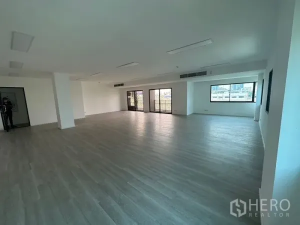 办公空间 出租 - 空置办公室的广角视图，中央立柱、吊顶空调出风口、木纹地板与多面采光窗。