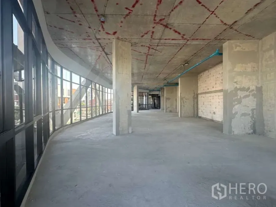 零售空间 出租在Phra Khanong, Bangkok - 长形开放商铺，左侧整面玻璃立面，立柱与毛坯地面。