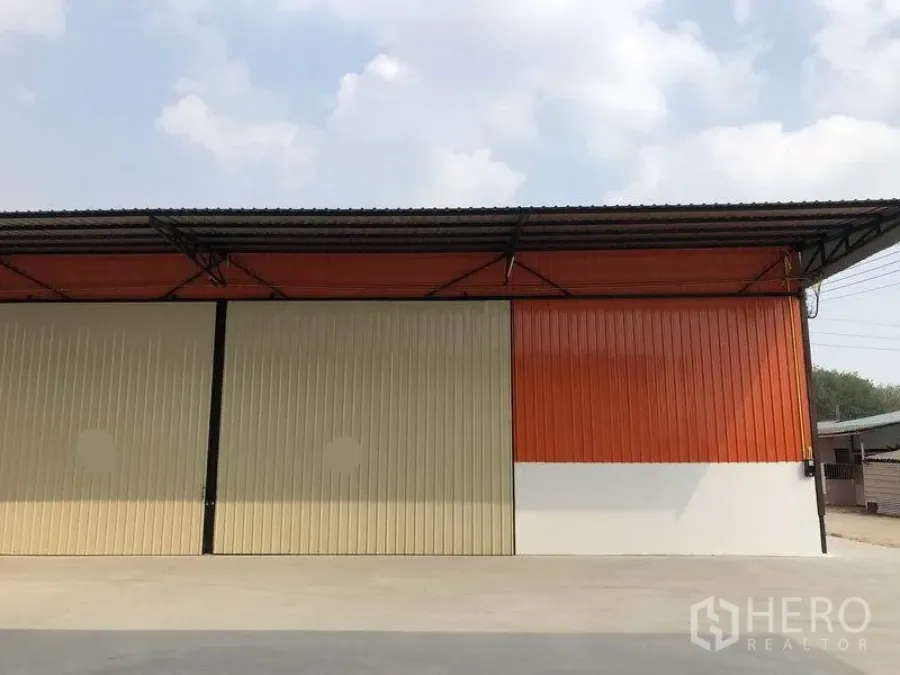 คลังสินค้า ให้เช่าในPathum Thani - ด้านนอกโกดัง ผนังสีส้ม ประตูบานเลื่อนปิด และลานคอนกรีตกว้าง