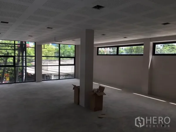 零售空间 出租在Huai Khwang, Bangkok - 开放式零售楼层，转角大玻璃窗，可见街景与绿树。