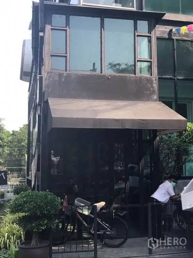 零售空间 出租在Watthana, Bangkok - 通罗区玻璃门面零售铺，黑色金属框架与遮蓬，绿植点缀，醒目外观。