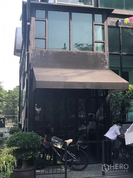 零售空间 出租在Watthana, Bangkok - 通罗区玻璃门面零售铺，黑色金属框架与遮蓬，绿植点缀，醒目外观。