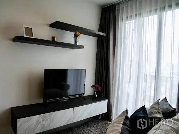 Condominium for rent in Pathum Wan, Bangkok - TV console with floating shelves and sheer floor-to-ceiling curtains opening to a city-view balcony.