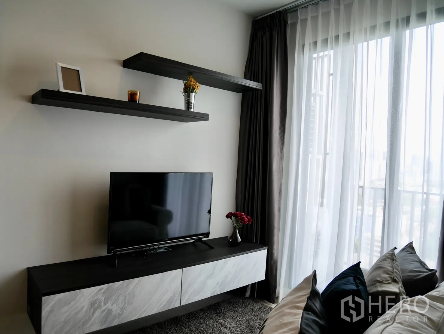 Condominium for rent in Pathum Wan, Bangkok - TV console with floating shelves and sheer floor-to-ceiling curtains opening to a city-view balcony.