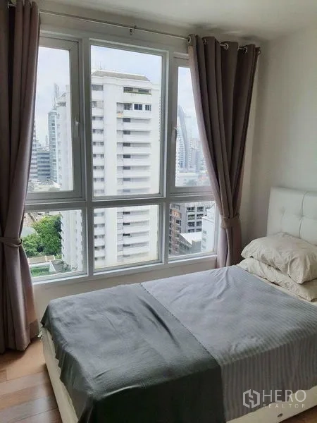 Condominium for rent in Watthana, Bangkok - Sunlit bedroom with large windows, curtains and city skyline view in a Watthana condo.