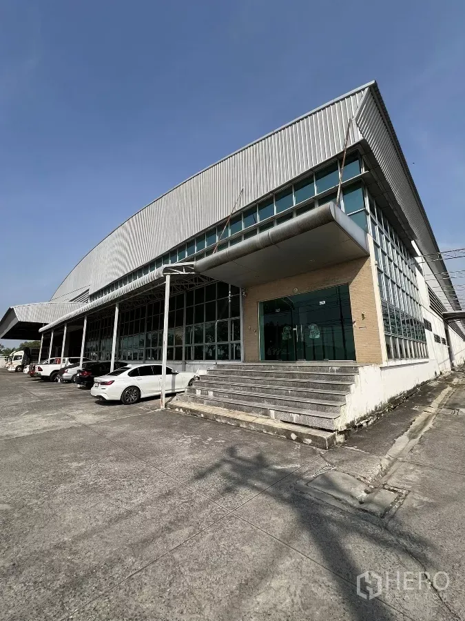 工厂 出租或出售在Sai Noi, Nonthaburi - 工厂外观，金属板墙体配玻璃立面办公区，前方有停车区