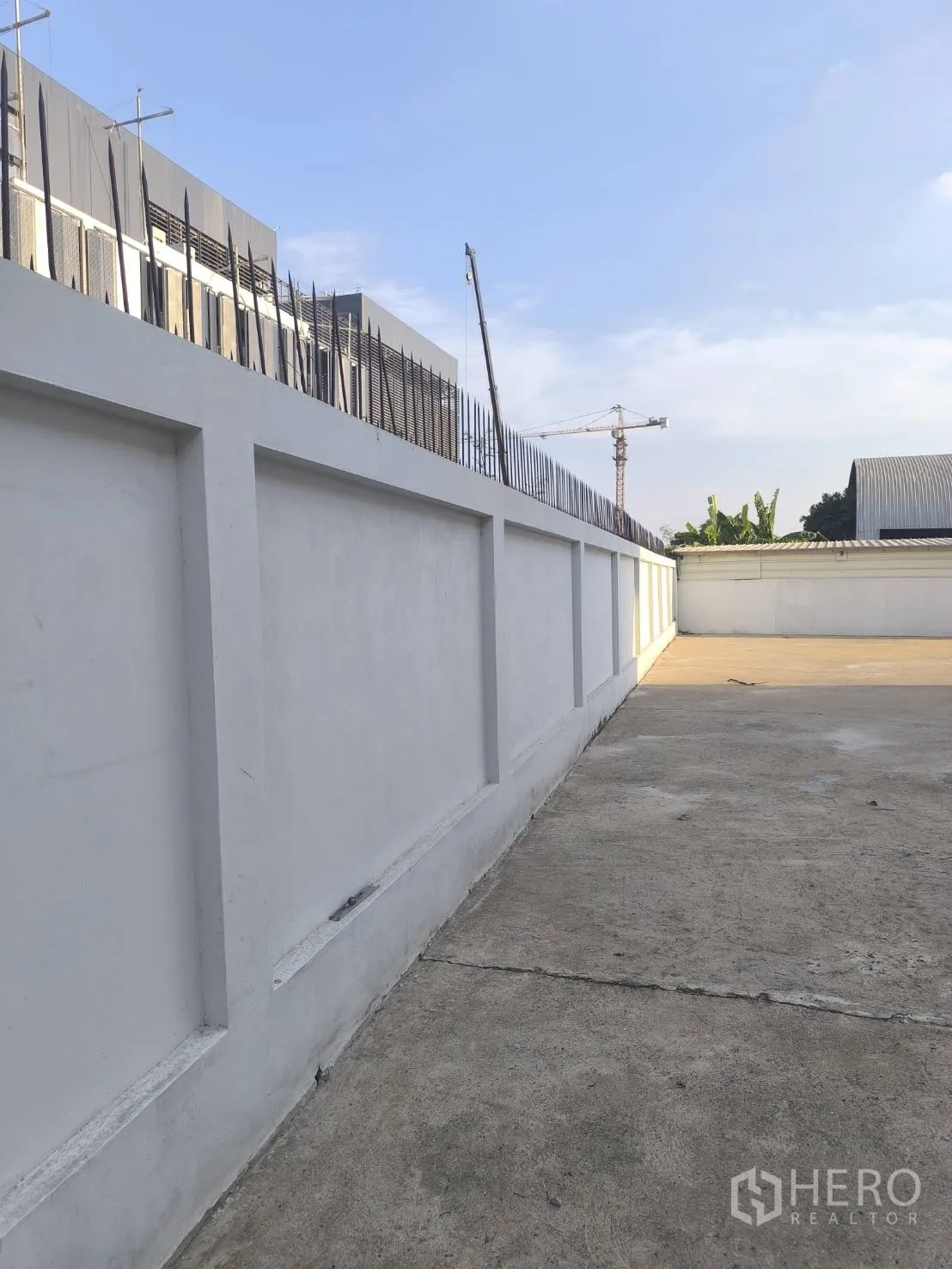 Factory for sale in Khlong Luang, Pathum Thani - Long side walkway along the walled boundary with spikes.