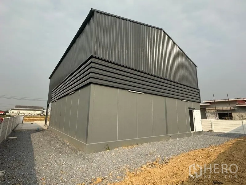 工厂 出租或出售在Bang Bua Thong, Nonthaburi - 钢板外墙仓库的后侧与侧面，可见通风带与碎石小径。