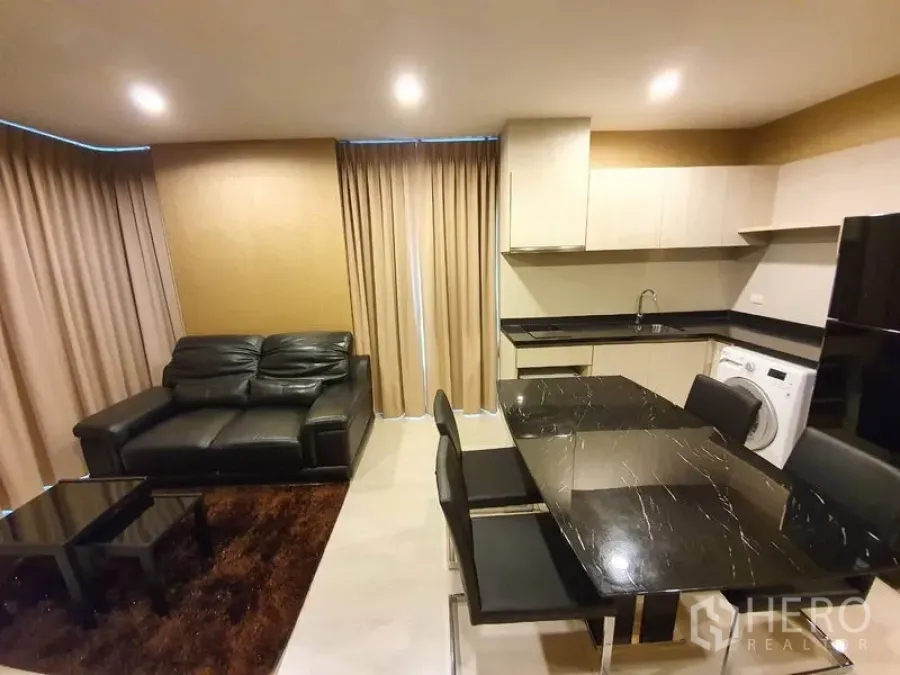 公寓 出租在Sathon, Bangkok - 开放式客厅与厨房，黑色石面餐桌、皮沙发、米色窗帘，配备橱柜、洗衣机和冰箱。