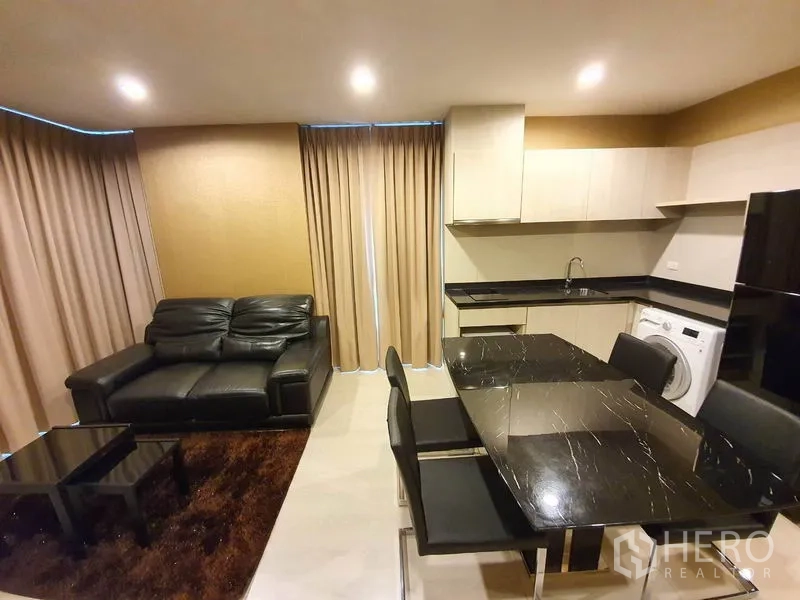 公寓 出租在Sathon, Bangkok - 开放式客厅与厨房，黑色石面餐桌、皮沙发、米色窗帘，配备橱柜、洗衣机和冰箱。