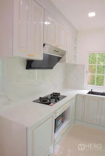 Detached House for rent in Bang Phli, Samut Prakan - L-shaped white kitchen with gas hob, hood and ample cabinetry.