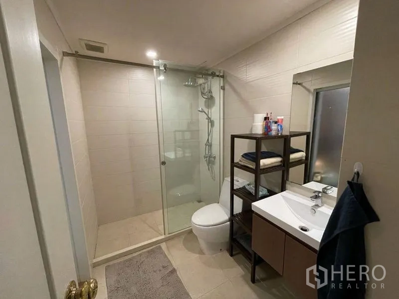 Condominium for sale in Watthana, Bangkok - Contemporary bathroom with glass-enclosed shower, vanity and toilet.