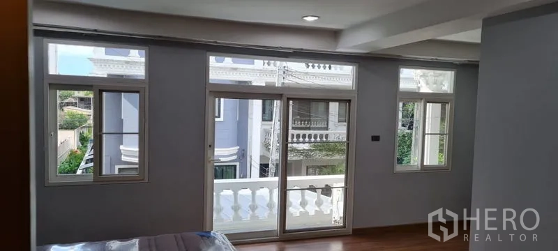 Townhouse for rent in Watthana, Bangkok - Bedroom view to a balcony through sliding glass doors and multiple windows.
