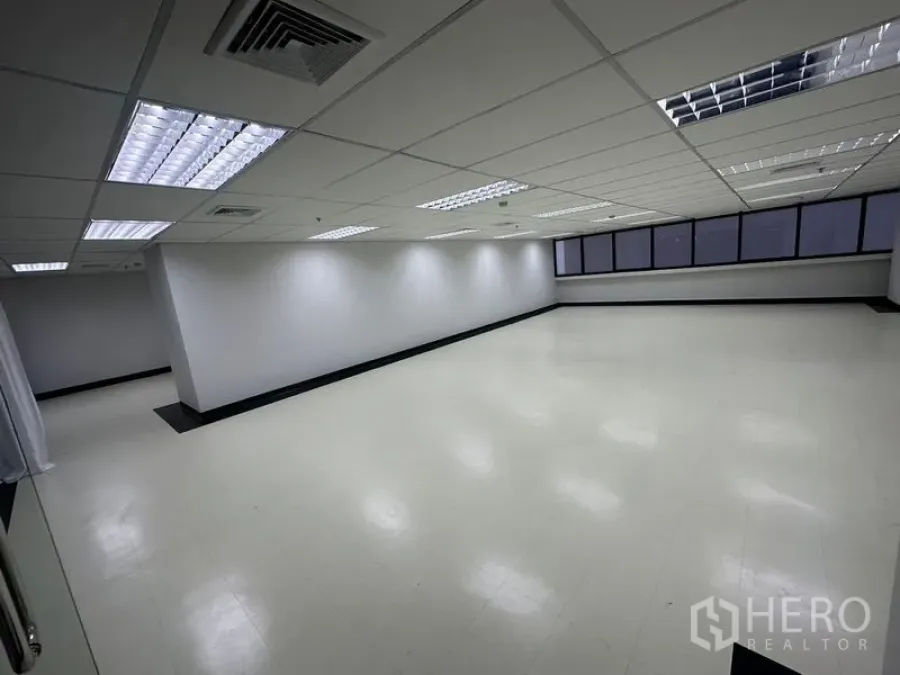 Office Space for rent - Open-plan 136 sq.m office interior in Ratchathewi, Bangkok with drop ceiling, fluorescent lights and a long window line.