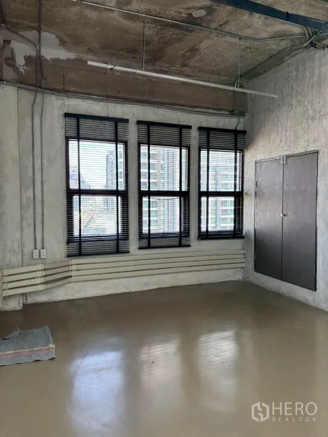 Office Space for rent in Watthana, Bangkok - Row of black-framed windows with city outlooks and a utility cabinet on concrete walls.